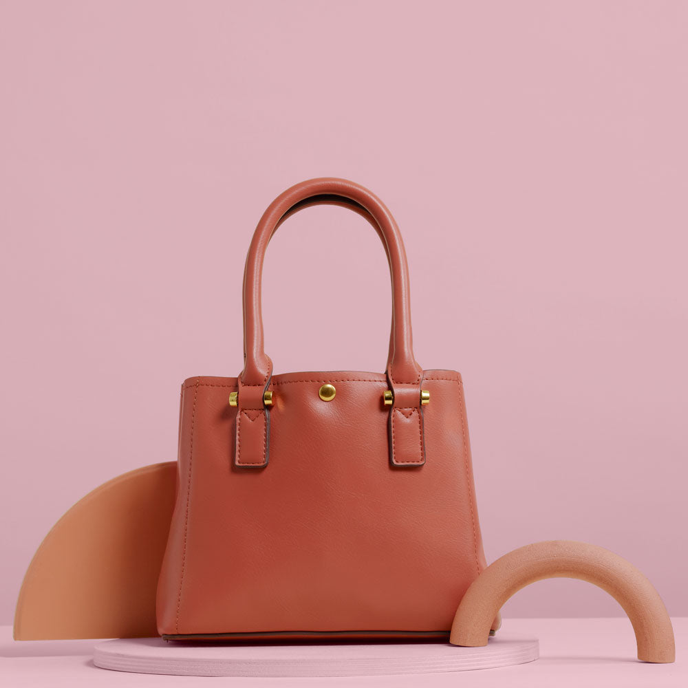 A still image of a small rose recycled vegan leather crossbody handbag against a pink wall with pink props. 