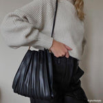 Model wearing a black pleated vegan leather shoulder bag. 