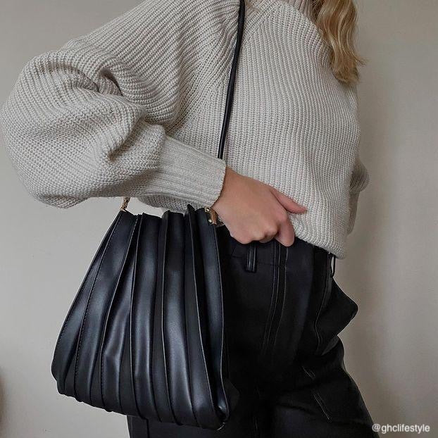 Model wearing a black pleated vegan leather shoulder bag. 