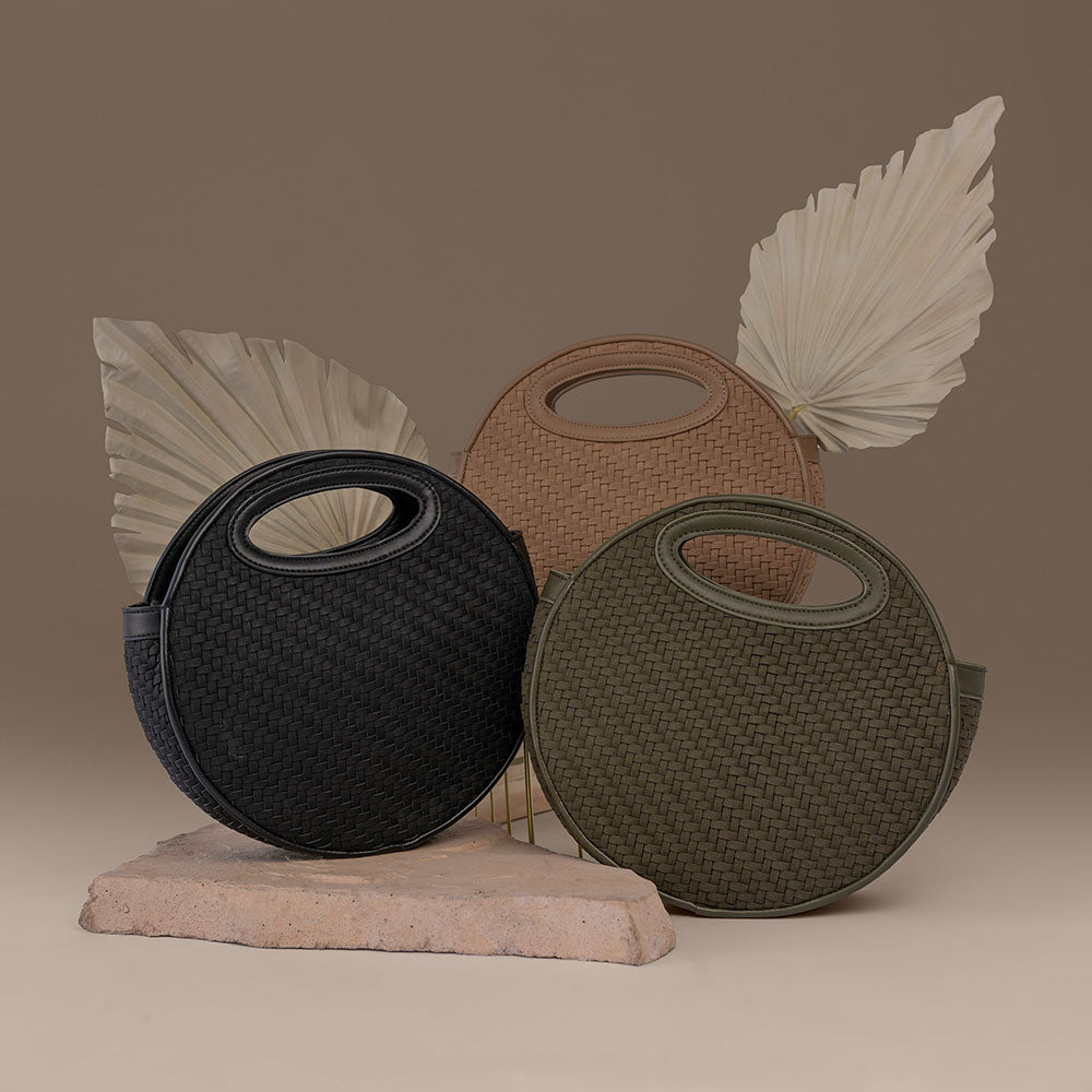 A still image of three circle shaped vegan leather crossbody bag with woven pattern against a brown wall.
