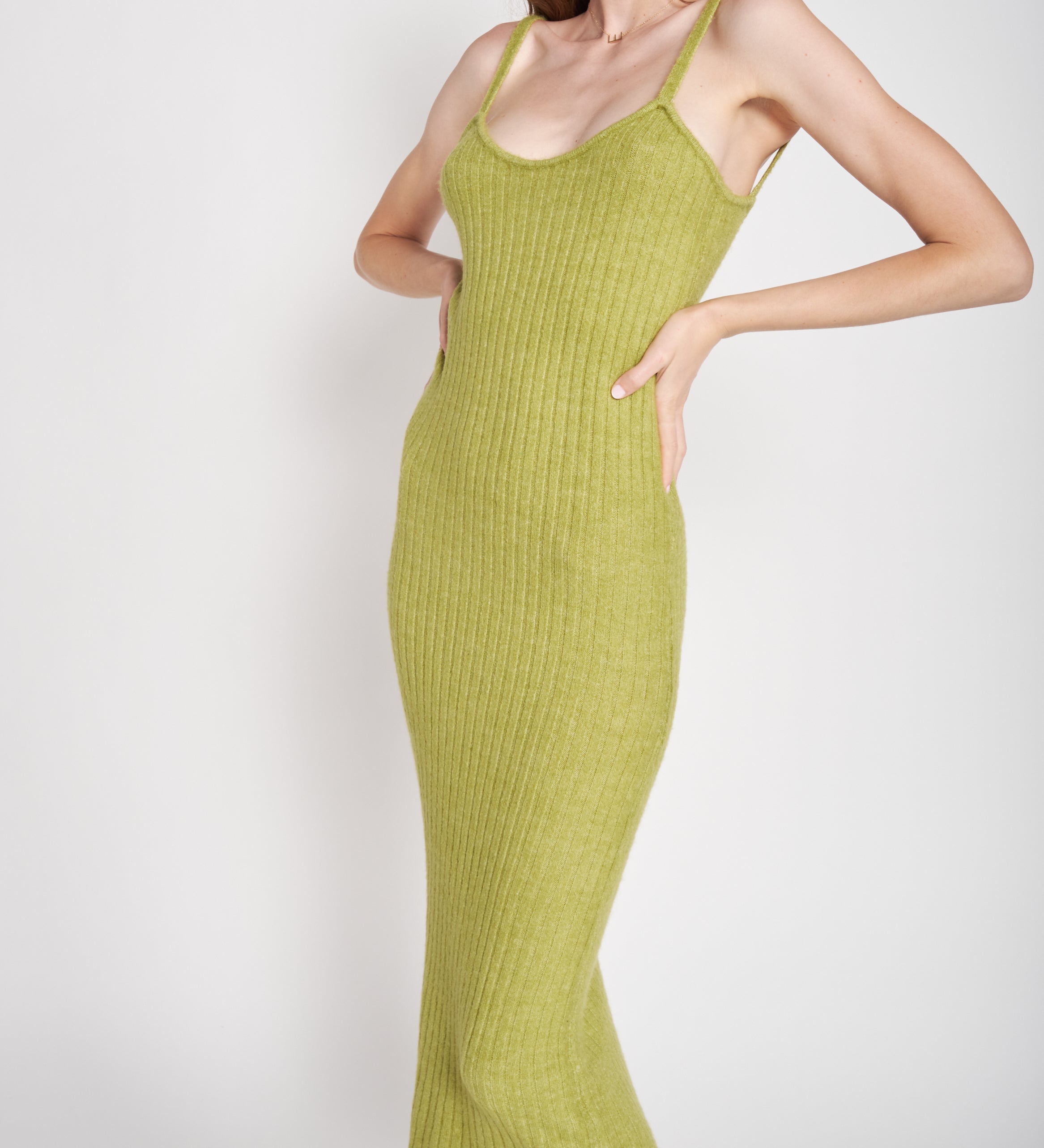 A model wearing a green midi dress against a white wall. 