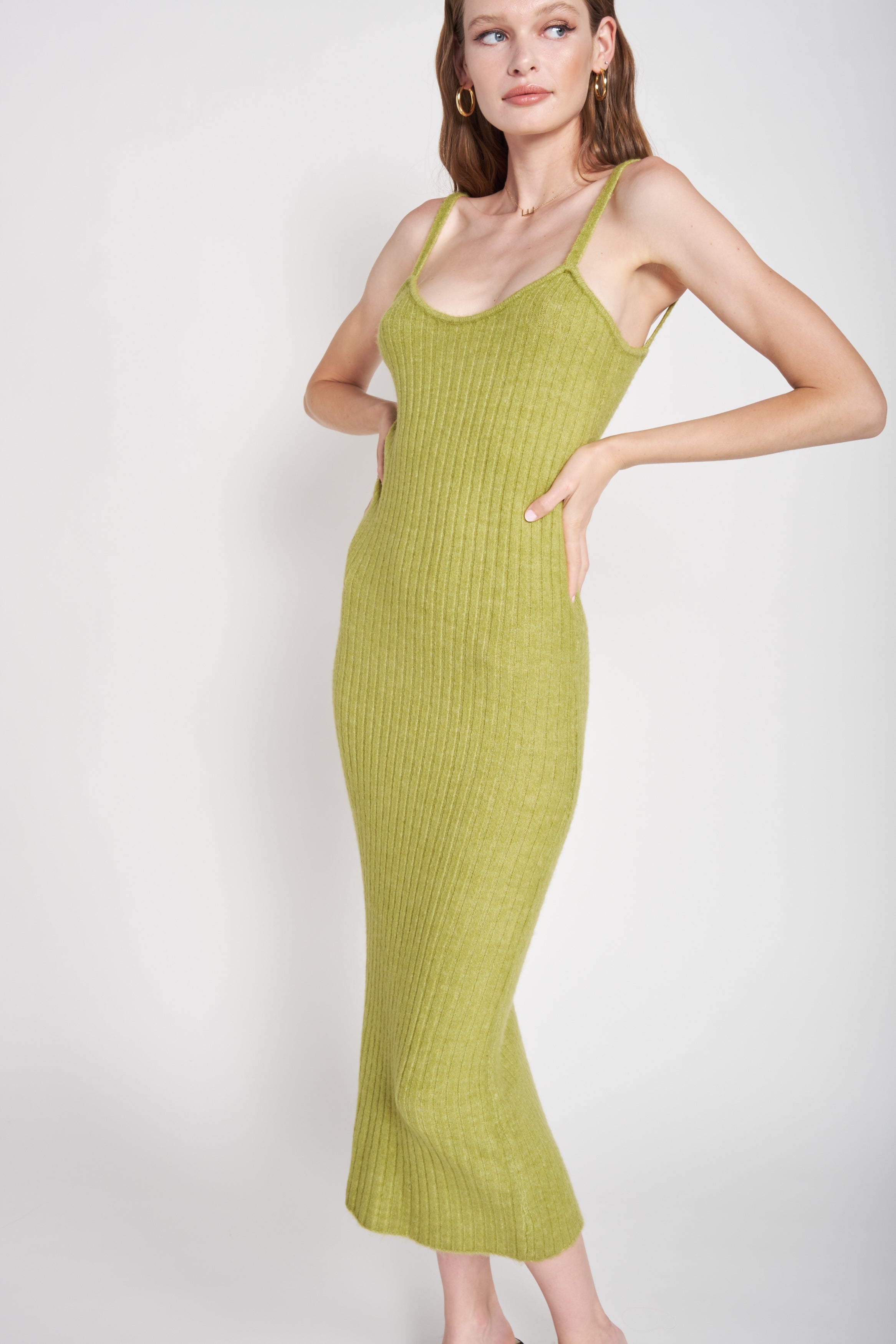 A model wearing a green midi dress against a white wall. 