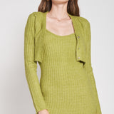 A model wearing a green two piece cardigan and midi dress set against a white wall.
