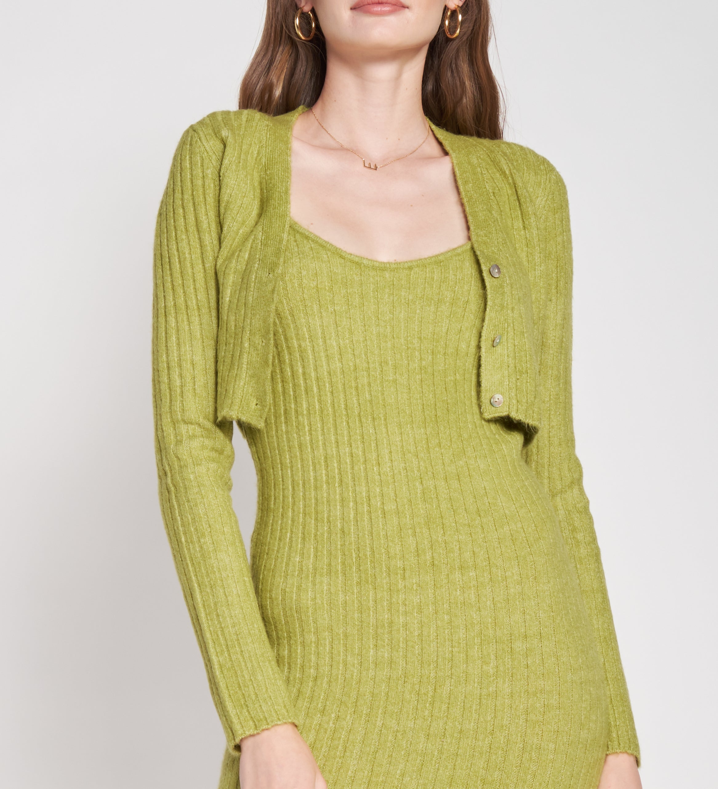 A model wearing a green two piece cardigan and midi dress set against a white wall.