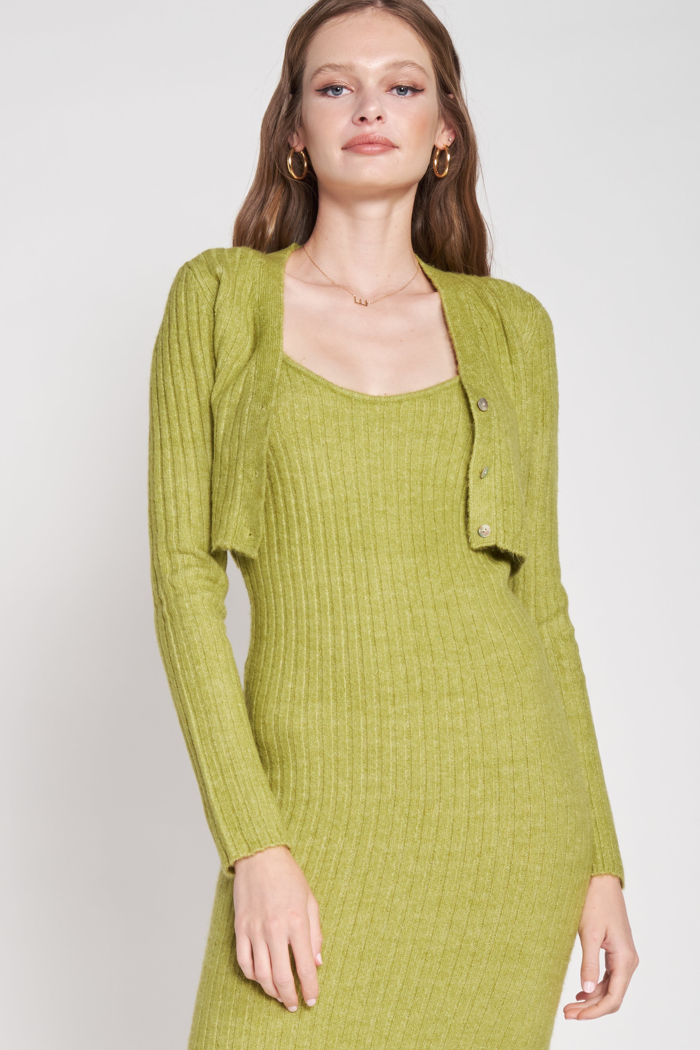 A model wearing a green two piece cardigan and midi dress set against a white wall.