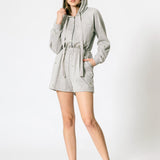 a model wearing a grey terry hooded romper against a white wall. 