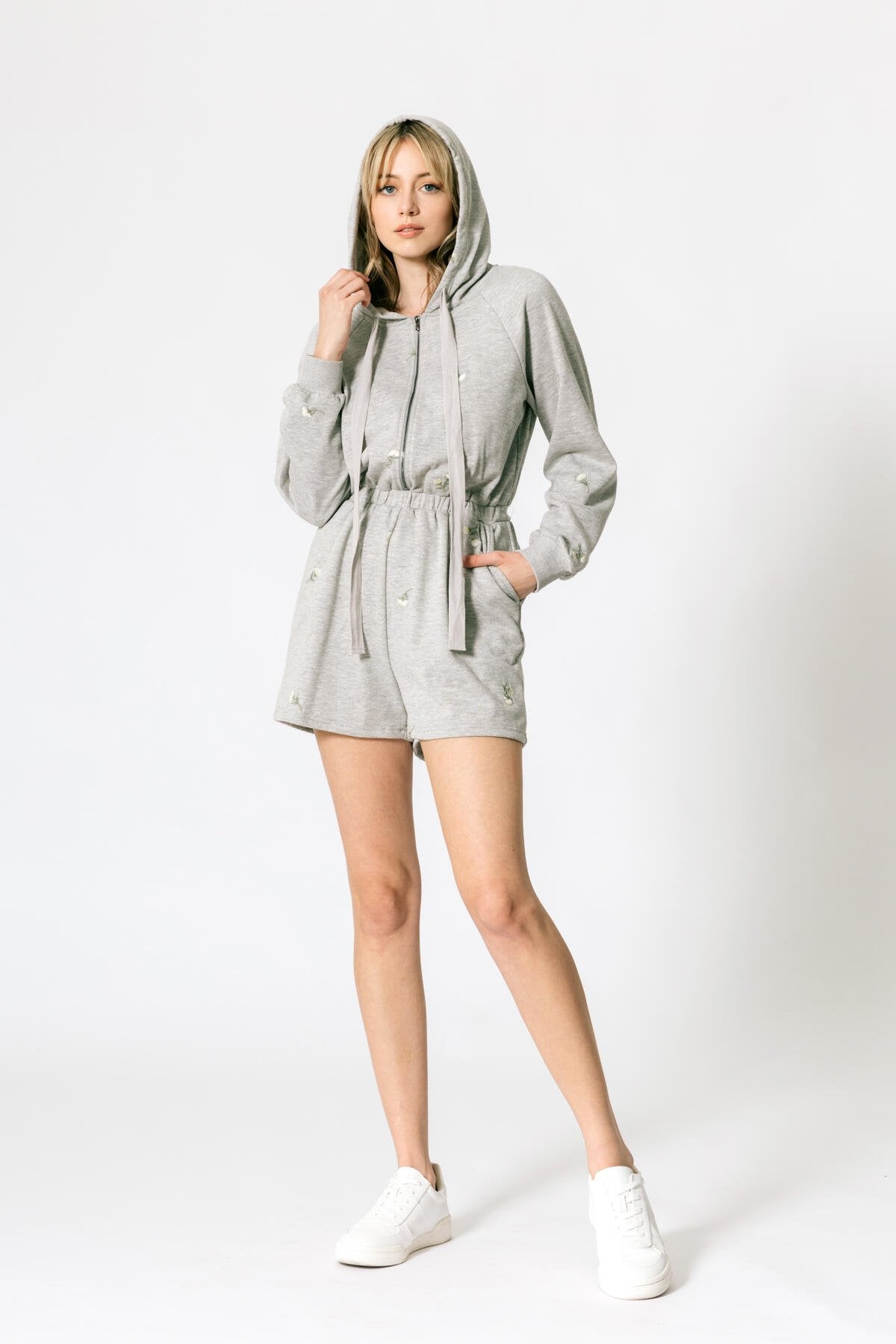 a model wearing a grey terry hooded romper against a white wall. 