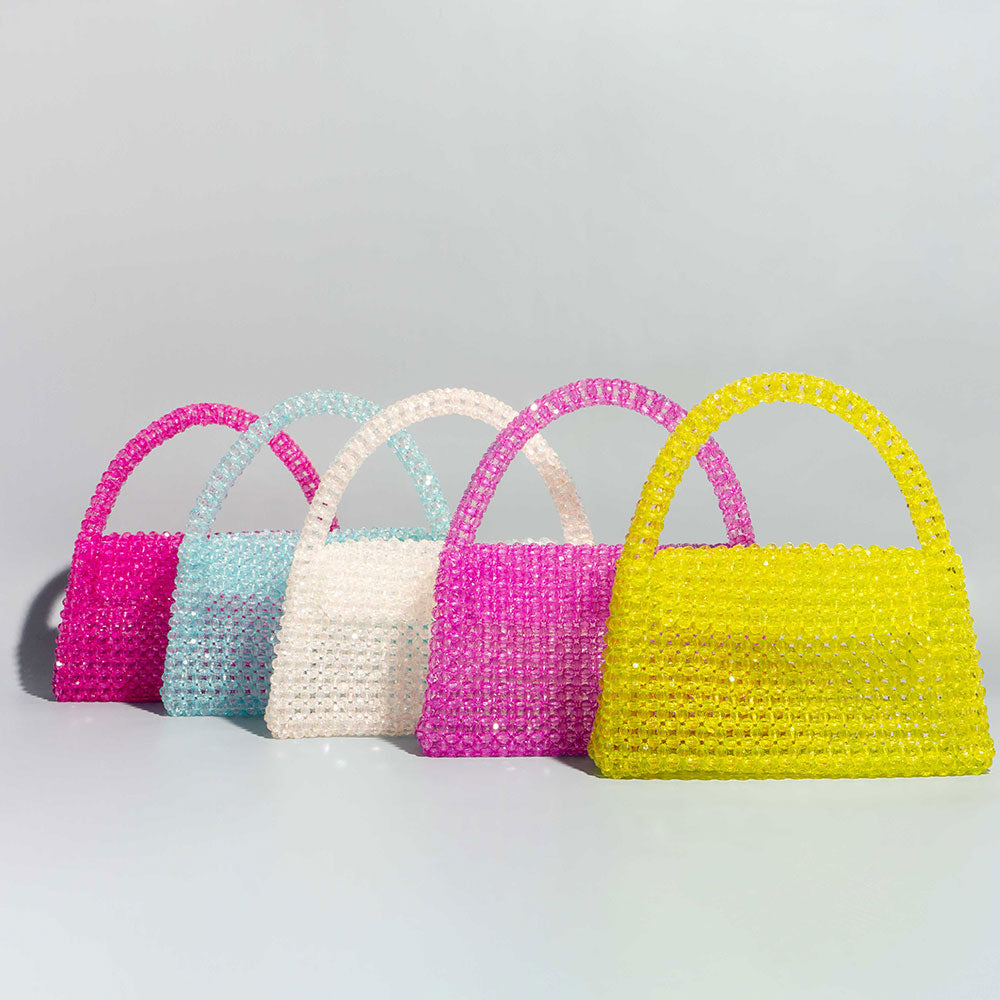 A still image of five different crystal beaded top handle bag with a flap closure against a blue wall. 