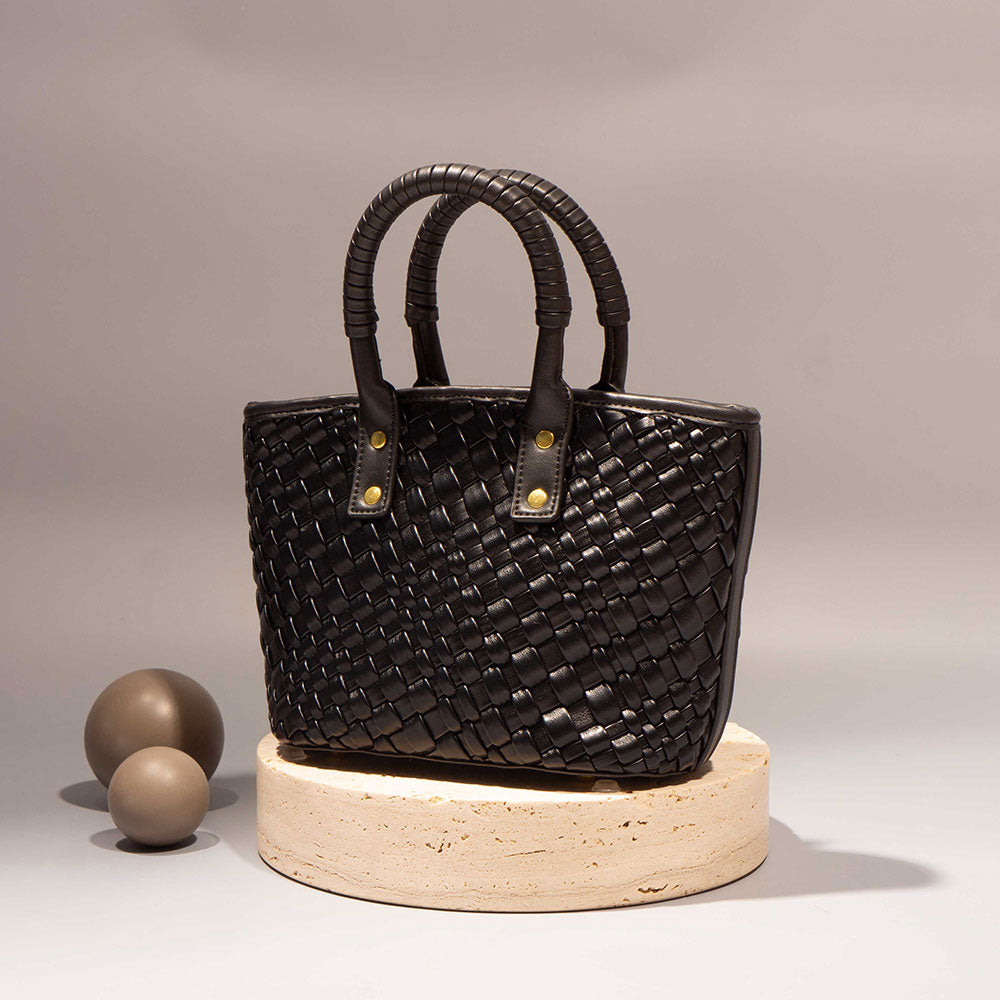 A still image of a small black crossbody bag with wrapped handle against a brown wall. 